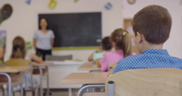 Een gelukkige jongen die tijdens de les in een schoolbureau zit en naar de camera kijkt.Leerproces op school. — Stockvideo
