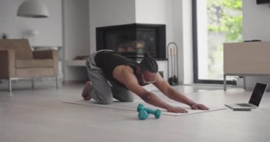 Afro-Amerikan atletik adam dizüstü bilgisayarda online eğitim dersleri izliyor, eğitmenden sonra hareketleri tekrarlıyor, evde bacak egzersizleri yapıyor. Kendini soyutlama. Karantina.
