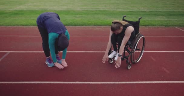 Tekerlekli sandalyede ısınan engelli bir kadın atletizm antrenmanında başörtüsü giyen Müslüman bir kadınla. — Stok video