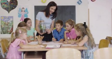 İlkokulda biyoloji sınıfında çocuklu bir bayan öğretmen biyoloji ya da sürdürülebilir bitkilerle ilgili botanik bilimsel deney yapıyor. Bitkileri bir bardakta öğrenmek.