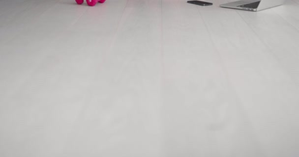 Sportovní žena ve sportovním oblečení sedí na podlaze s činkami a proteinovým koktejlem nebo lahví vody a doma v obývacím pokoji používá notebook. Sportovní a rekreační koncept. — Stock video