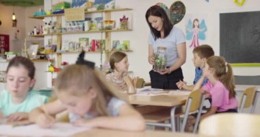 İlkokulda biyoloji sınıfında çocuklu bir bayan öğretmen biyoloji ya da sürdürülebilir bitkilerle ilgili botanik bilimsel deney yapıyor. Bitkileri bir bardakta öğrenmek.