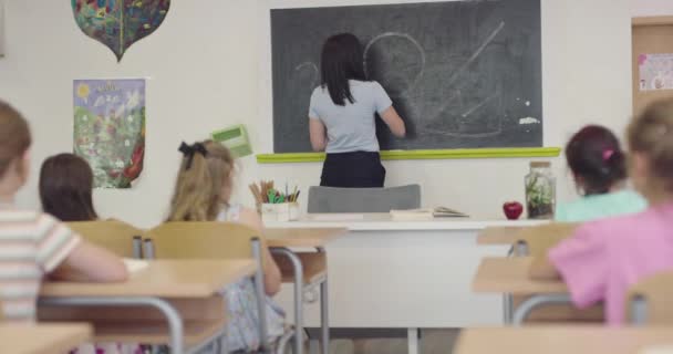 Lernprozess in der Schule, Lehrerin schreibt mit Kreide auf die Tafel. — Stockvideo