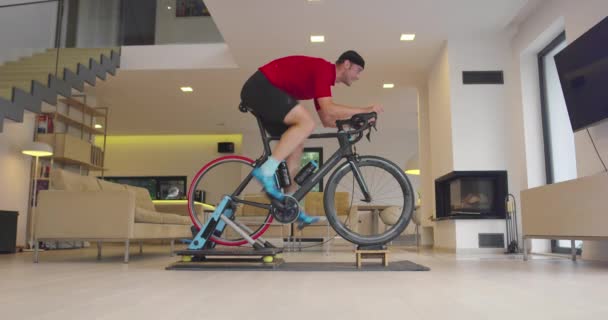 Bisikletli bir adam evde egzersiz yapıyor. Coronavirus Covid19 tecridi sırasında çevrimiçi bisiklet yarışı oynuyor. Yeni normal kavram. — Stok video