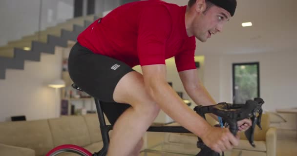 Homem de bicicleta no treinador de máquina que ele está exercendo na casa.Jogando jogo de corrida de bicicleta on-line durante coronavírus covid19 lockdown. Novo conceito normal. — Vídeo de Stock