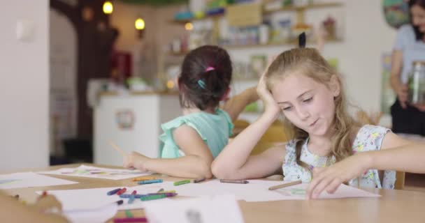 Crianças pintando na sala de jogos. Duas meninas desenhando sobre papel na mesa em sala de aula. — Vídeo de Stock