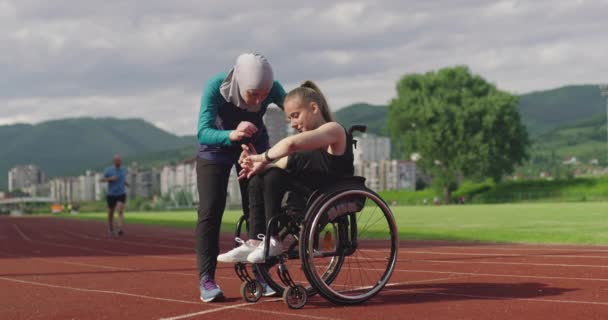 Group of multi cultural sports people disabled female and her trainer wearing hijab after training on athletics sports track checking data on a smartwatch. — Stock Video