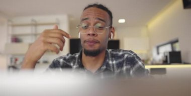 Afro-Amerikalı iş adamı akıllı telefon ve laptop kullanarak online konferans videosu çekiyor. Erkek çağrı merkezi ajanı, yönetici modern bir ev ofisinde web kamerası toplantısı yapıyor.