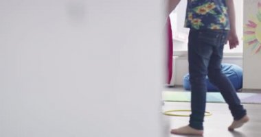 Küçük anaokulu öğrencileri ve bayan öğretmenleri sınıfın içinde egzersiz yapıyorlar. Hula hoop çemberinin üzerinden zıplarken yerde.