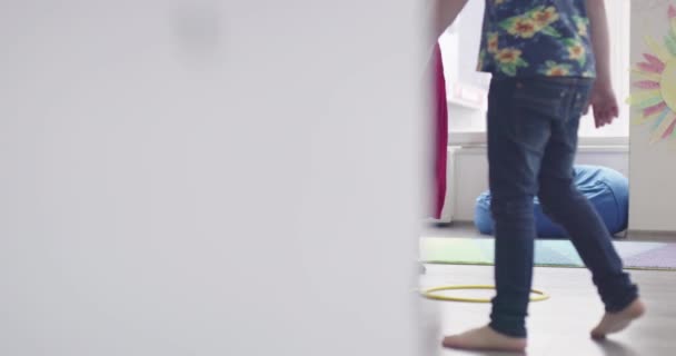 Pequeños niños de guardería con maestra en el suelo en el aula, haciendo ejercicio. Saltar sobre la pista círculos hula hoop en el suelo. — Vídeos de Stock