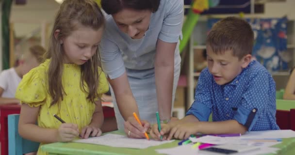 Kreative Kinder während eines Kunstkurses in einer Kindertagesstätte oder Grundschule zeichnen mit einer Lehrerin. — Stockvideo