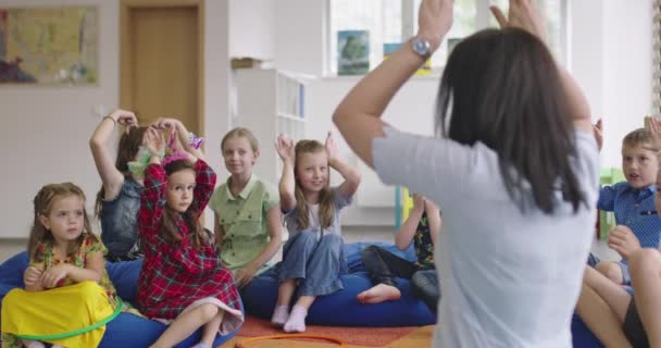 Professeur d'école élémentaire ou primaire lisant une histoire à un groupe d'enfants dans une garderie. — Video