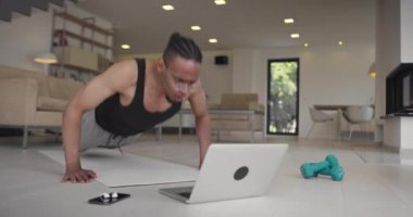 Sıkı çalışma. Bitkin bir adam. Zayıf eller. Online eğitim. Evde spor salonu. Yorgun adam yumruklarıyla şınav çekiyor. Dizüstü bilgisayarı görüyor. Yoga minderinden düşüyor..