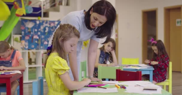 Kreative Kinder während eines Kunstkurses in einer Kindertagesstätte oder Grundschule zeichnen mit einer Lehrerin. — Stockvideo