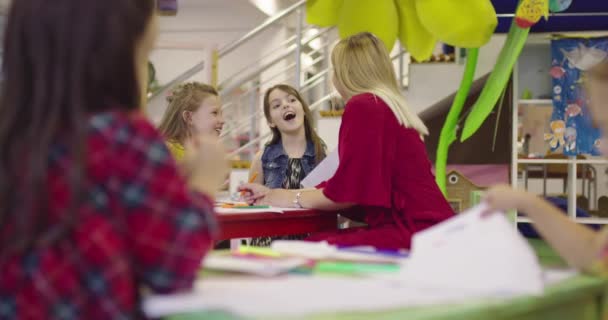 I grundskolan barn ritar i klassrummet med en kvinnlig lärare, tillsammans leende. Långsamma rörelser — Stockvideo