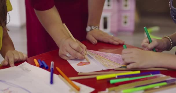 Creative kids during an art class in a daycare center or elementary school classroom drawing with female teacher. — Stock Video