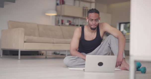 African American γυμναστής γυμναστήριο χρησιμοποιώντας φορητό υπολογιστή για online εκπαίδευση με τον πελάτη κατά τη διάρκεια της πανδημίας coronavirus. — Αρχείο Βίντεο