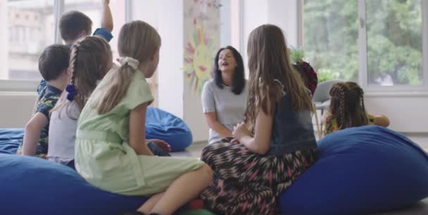 Storytime elementary or primary school teacher reading a story to a group of children in a daycare center. — Stock Video