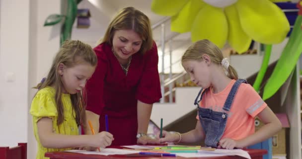 Kreative Kinder während eines Kunstkurses in einer Kindertagesstätte oder Grundschule zeichnen mit einer Lehrerin. — Stockvideo