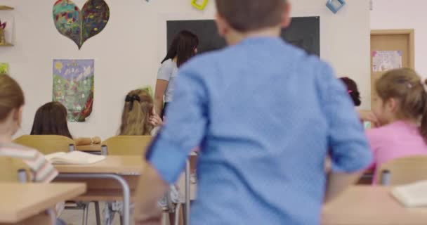 Leraar stelde haar leerlingen een vraag op de basisschool en kind jongen stak zijn hand op om het antwoord op het bord te schrijven. Leerproces op school. — Stockvideo