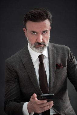 Yetişkin iş adamının son moda takım elbiseli portresi ve modern stüdyoda siyah arka planda şık bir sandalyede oturuyor.