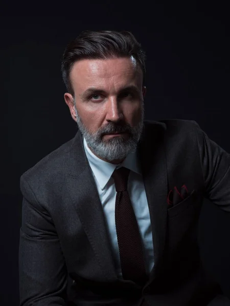 Retrato de un elegante y elegante hombre de negocios con barba y ropa de negocios casual en un estudio fotográfico aislado sobre un fondo oscuro con las manos — Foto de Stock