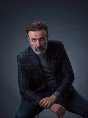 Yetişkin iş adamının son moda takım elbiseli portresi ve modern stüdyoda siyah arka planda şık bir sandalyede oturuyor.