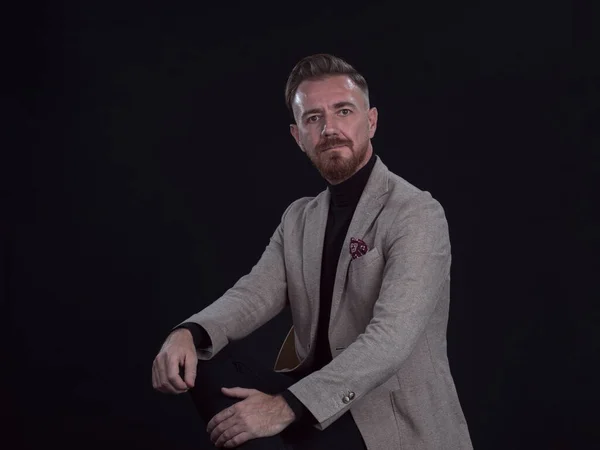 Retrato de un hombre de negocios adulto con traje de moda y sentado en un estudio moderno en una silla elegante contra el fondo negro Fotos de stock libres de derechos