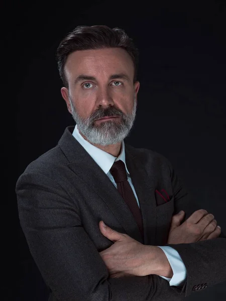 Portret van een stijlvolle elegante senior zakenman met een baard en casual zakelijke kleding in fotostudio geïsoleerd op donkere achtergrond gebaren met handen — Stockfoto