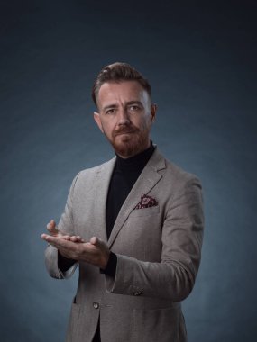 Fotoğraf stüdyosunda sakallı ve sıradan iş kıyafetleri giyen zarif bir kıdemli işadamının portresi. Koyu renk arka planda el kol hareketleriyle izole edilmiş.