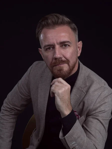 Portrait d'un homme d'affaires adulte vêtu d'un costume tendance et assis dans un studio moderne sur une chaise élégante sur fond noir — Photo