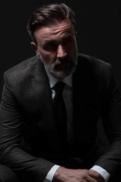 Portret eleganckiego starszego biznesmena z brodą i ubraniami biznesowymi w studiu fotograficznym odizolowanego na ciemnym tle gestykulującego dłońmi — Zdjęcie stockowe