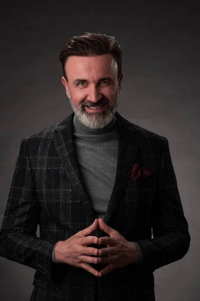 Retrato de un elegante y elegante hombre de negocios con barba y ropa de negocios casual en un estudio fotográfico aislado sobre un fondo oscuro con las manos — Foto de Stock