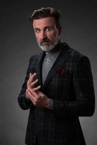 Retrato de un elegante y elegante hombre de negocios con barba y ropa de negocios casual en un estudio fotográfico aislado sobre un fondo oscuro con las manos — Foto de Stock