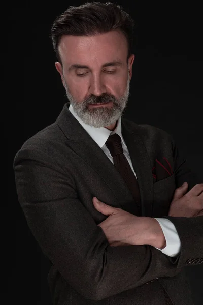Portret eleganckiego starszego biznesmena z brodą i ubraniami biznesowymi w studiu fotograficznym odizolowanego na ciemnym tle gestykulującego dłońmi — Zdjęcie stockowe