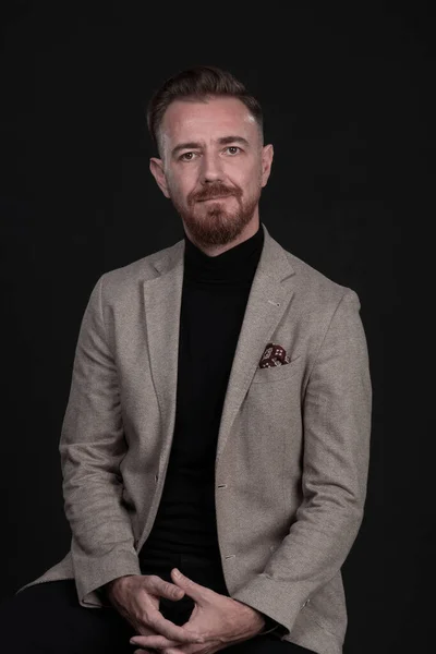 Retrato de un hombre de negocios adulto con traje de moda y sentado en un estudio moderno en una silla elegante contra el fondo negro — Foto de Stock