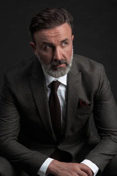 Retrato de um elegante homem de negócios sênior elegante com barba e roupas de negócios casuais em estúdio de fotografia isolado em fundo escuro gesticulando com as mãos — Fotografia de Stock