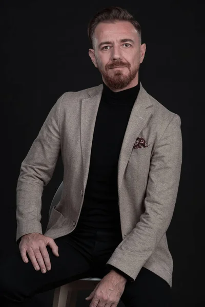 Retrato de un hombre de negocios adulto con traje de moda y sentado en un estudio moderno en una silla elegante contra el fondo negro — Foto de Stock