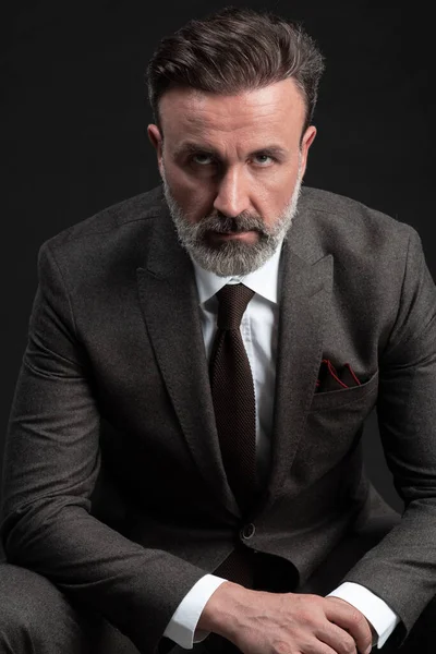 Retrato de un elegante y elegante hombre de negocios con barba y ropa de negocios casual en un estudio fotográfico aislado sobre un fondo oscuro con las manos — Foto de Stock