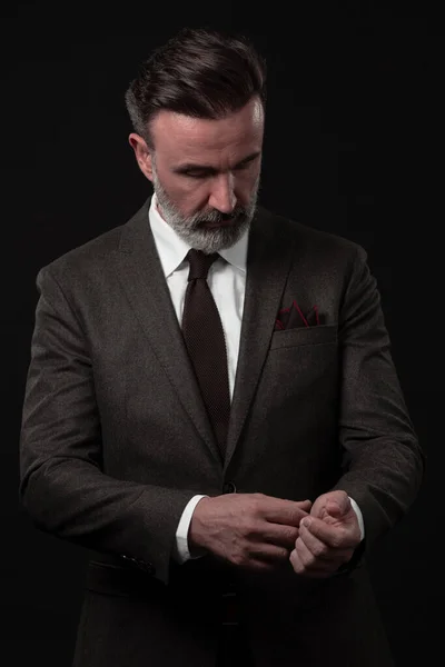 Retrato de um elegante homem de negócios sênior elegante com barba e roupas de negócios casuais em estúdio de fotos ajustando terno — Fotografia de Stock