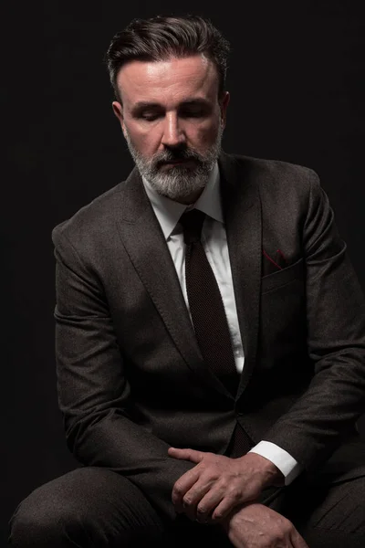 Portrait of a stylish elegant senior businessman with a beard and casual business clothes in photo studio isolated on dark background gesturing with hands — Stock Photo, Image