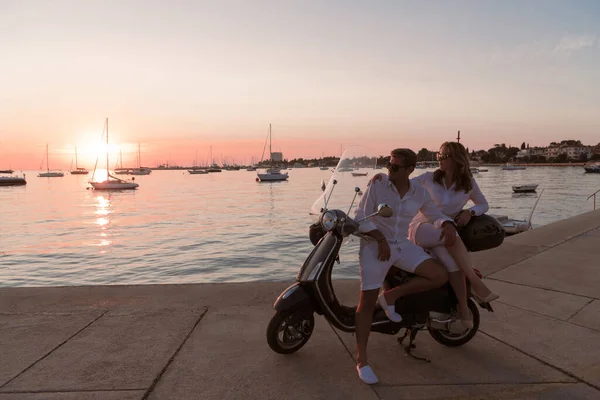 O casal desfruta de férias enquanto se senta em uma scooter à beira-mar e desfruta do belo nascer do sol. Foco seletivo — Fotografia de Stock