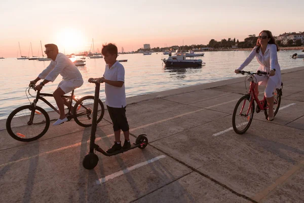 Gelukkig gezin genietend van een prachtige ochtend aan zee samen, ouders die fietsen en hun zoon die op een elektrische scooter rijdt. Selectieve focus — Stockfoto