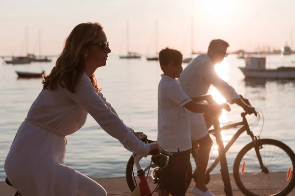 Joyeux famille profitant d'une belle matinée au bord de la mer ensemble, les parents en vélo et leur fils en scooter électrique. Concentration sélective — Photo