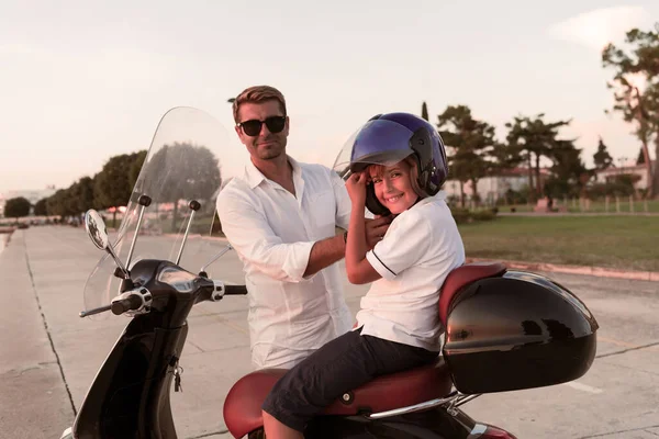 Um pai com seu filho desfruta de umas férias montando uma scooter junto ao mar no início da manhã. Foco seletivo — Fotografia de Stock