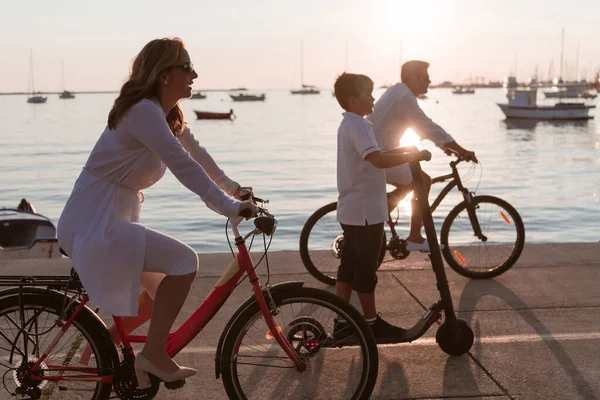Mutlu bir aile deniz kenarında güzel bir sabah geçiriyorlar, ebeveynler bisiklete biniyor ve oğulları elektrikli scooter kullanıyor. Seçici odak — Stok fotoğraf