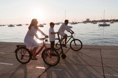 Mutlu bir aile deniz kenarında güzel bir sabah geçiriyorlar, ebeveynler bisiklete biniyor ve oğulları elektrikli scooter kullanıyor. Seçici odak 