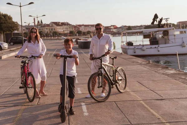 Lycklig familj njuter av en vacker morgon vid havet tillsammans, föräldrar rider en cykel och deras son rider en elektrisk skoter. Selektiv inriktning — Stockfoto