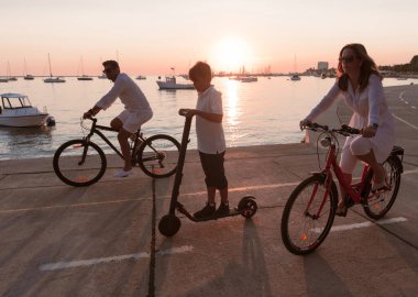 Mutlu bir aile deniz kenarında güzel bir sabah geçiriyorlar, ebeveynler bisiklete biniyor ve oğulları elektrikli scooter kullanıyor. Seçici odak 
