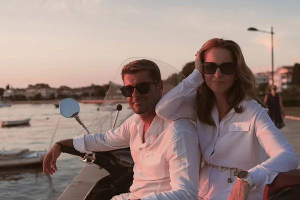 O casal desfruta de férias enquanto se senta em uma scooter à beira-mar e desfruta do belo nascer do sol. Foco seletivo — Fotografia de Stock
